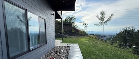 A modern house with large windows, a stone pathway, and a grassy yard with trees.