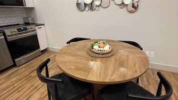 A dining area with a round wooden table, four black chairs, and a decorative wall piece above the table.