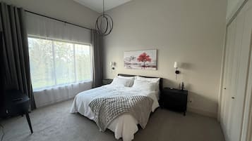 Une chambre à coucher avec un grand lit, une table de chevet, une lampe, un tableau au mur et une fenêtre avec des rideaux.