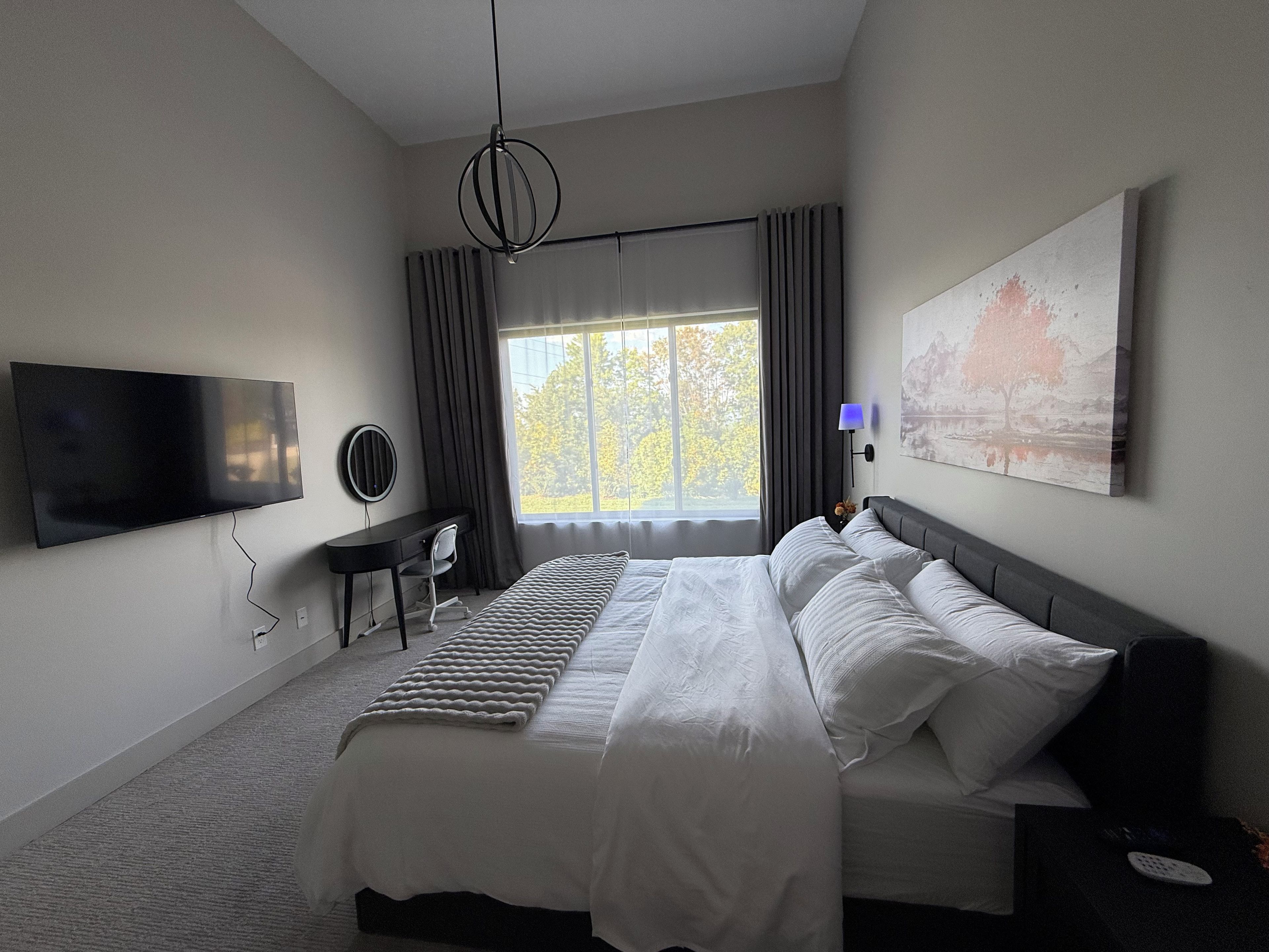 A modern hotel room with a large bed, a desk, a flat-screen TV, and a window with curtains.