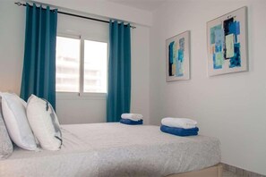 Een hotelkamer met een bed, twee kussens, een raam met gordijnen en twee abstracte schilderijen aan de muur.