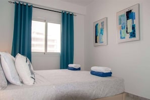 A hotel room with a bed, two pillows, a window with curtains, and two abstract paintings on the wall. - 2 apartments for up to 8 guests in Estoril beach (Sal Rei)