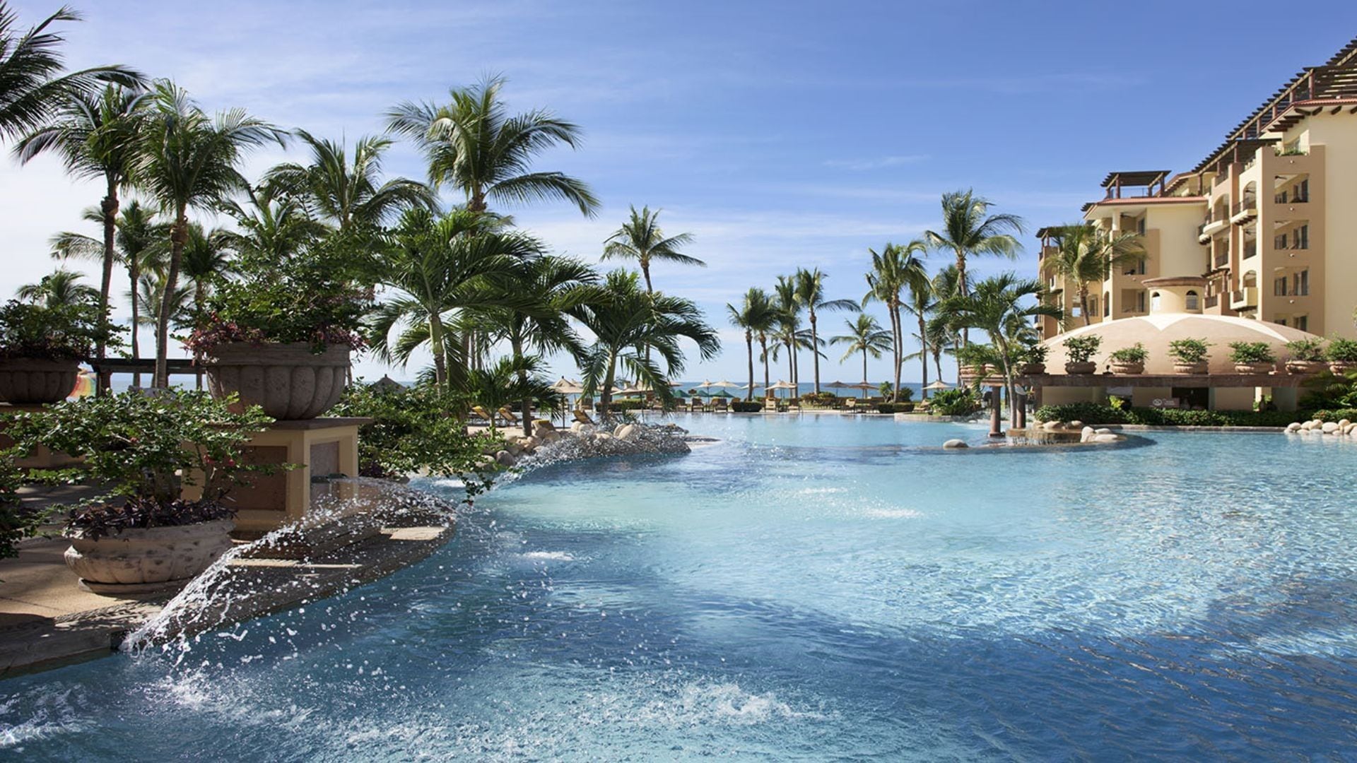 A resort pool with palm trees and a building with balconies.