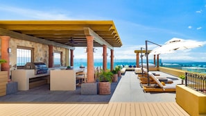 A rooftop terrace with a barbecue area, seating, and a view of the ocean. - Luxury 2BR Villa at Villa La Estancia – Stunning Views, Infinity Pools & Spa (Nuevo Nayarit)