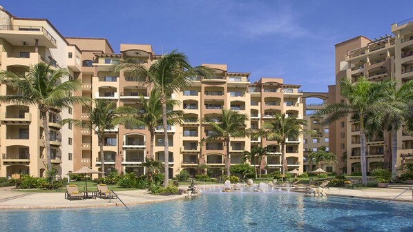 A hotel with multiple floors, balconies, and a swimming pool with lounge chairs and palm trees. - Luxury 2BR Villa at Villa La Estancia – Stunning Views, Infinity Pools & Spa (Nuevo Nayarit)