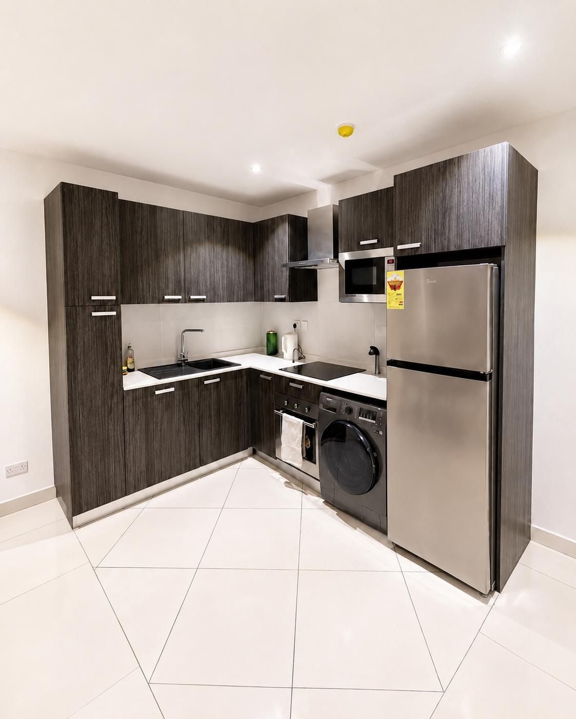 Une cuisine moderne avec des meubles en bois foncé, des appareils électroménagers en acier inoxydable et un sol carrelé de couleur blanche.