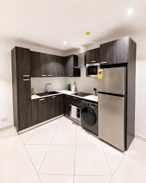 Una cocina moderna con gabinetes de madera oscura, electrodomésticos de acero inoxidable y piso de baldosas blancas.