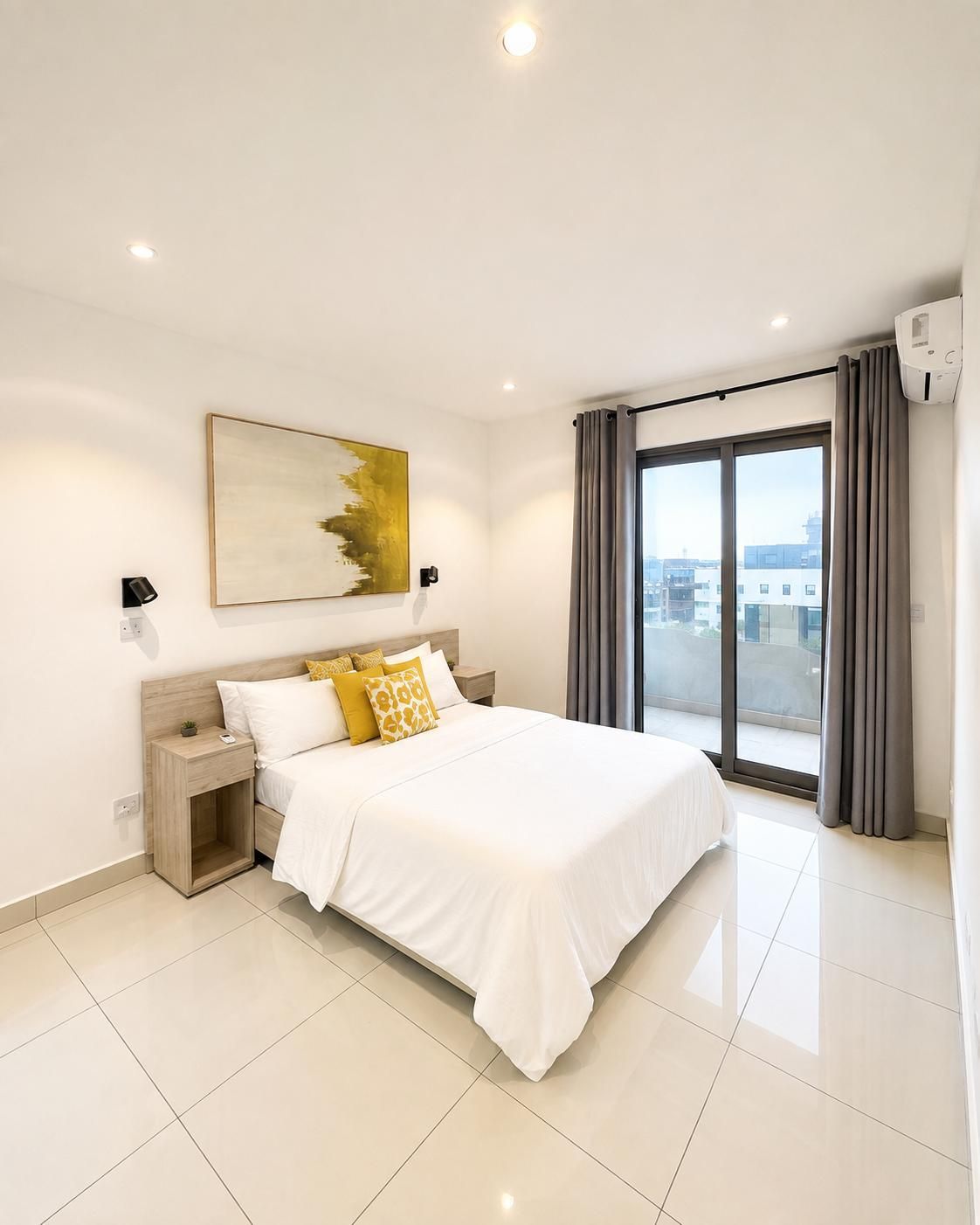 Une chambre moderne avec un grand lit, une table de chevet, une lampe fixée au mur, un luminaire au plafond, une fenêtre avec des rideaux et une vue sur la ville.