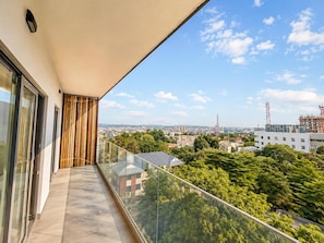 Un balcón con barandilla de vidrio que ofrece vistas a un paisaje urbano con edificios y árboles.