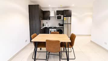 Een moderne keuken met donkere kasten, een koelkast van roestvrij staal en een houten eettafel met vier stoelen.