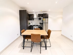 Una cocina moderna con armarios oscuros, un refrigerador de acero inoxidable y una mesa de comedor de madera con cuatro sillas.