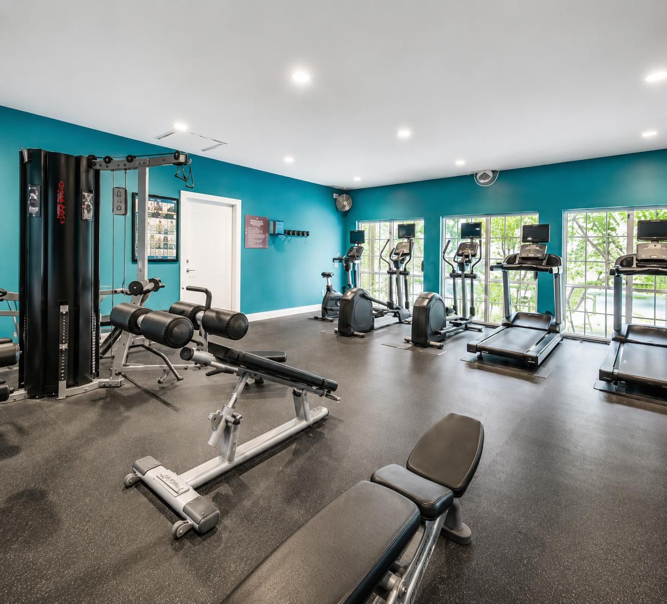 Une salle de sport équipée de matériel d’exercice, d’un banc et d’une fenêtre donnant sur un espace verdoyant.