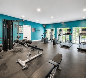 Un gimnasio con equipo de ejercicio, una banca y un ventanal con vistas a la vegetación.