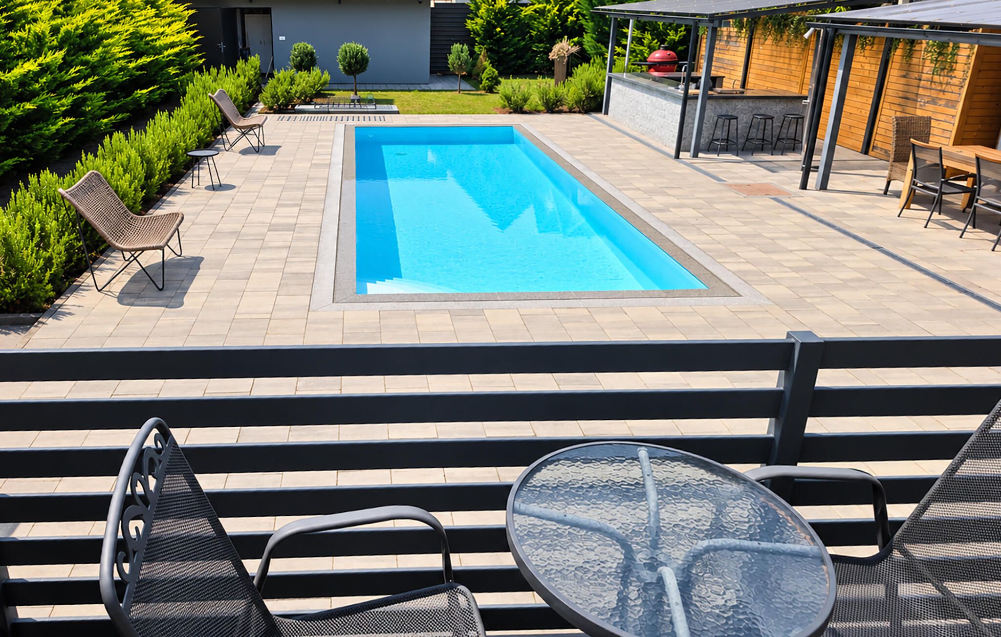 Une piscine avec un espace patio, des sièges d’extérieur et un barbecue.