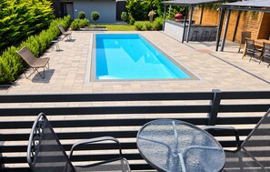 Une piscine avec un espace patio, des sièges d’extérieur et un barbecue.