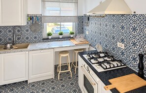 Une cuisine de taille réduite, équipée d’une cuisinière à gaz, d’un évier et d’une fenêtre agrémentée de plantes en pot.