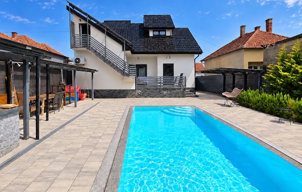 A residential property with a swimming pool, a covered patio area, and a staircase leading to a second floor.
