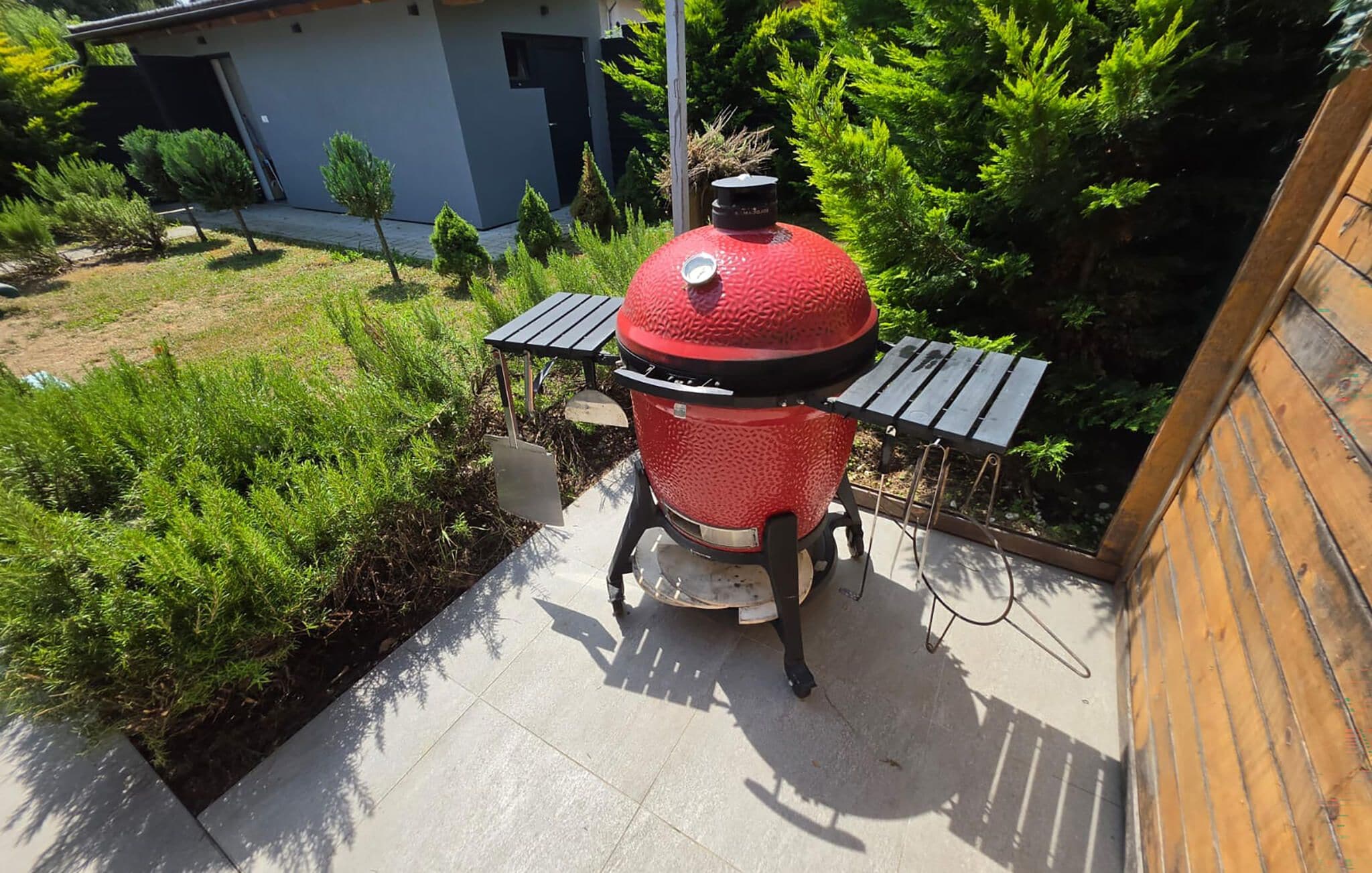 Un barbecue rouge avec un couvercle et deux petites tables d’appoint, installé sur une terrasse.