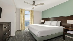 Habitación de hotel con cama, escritorio, cómoda, ventilador de techo y ventana con cortinas.