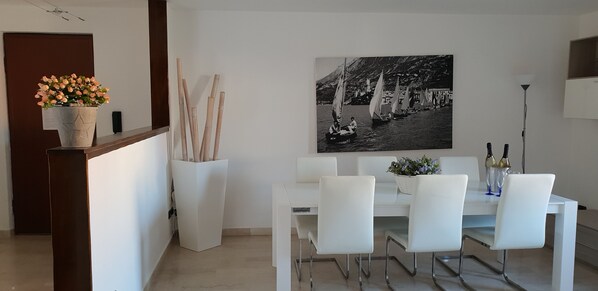 A dining area with a white table, four chairs, a vase with flowers, and a black and white photograph on the wall. - Apartment at the Port (Malcesine)