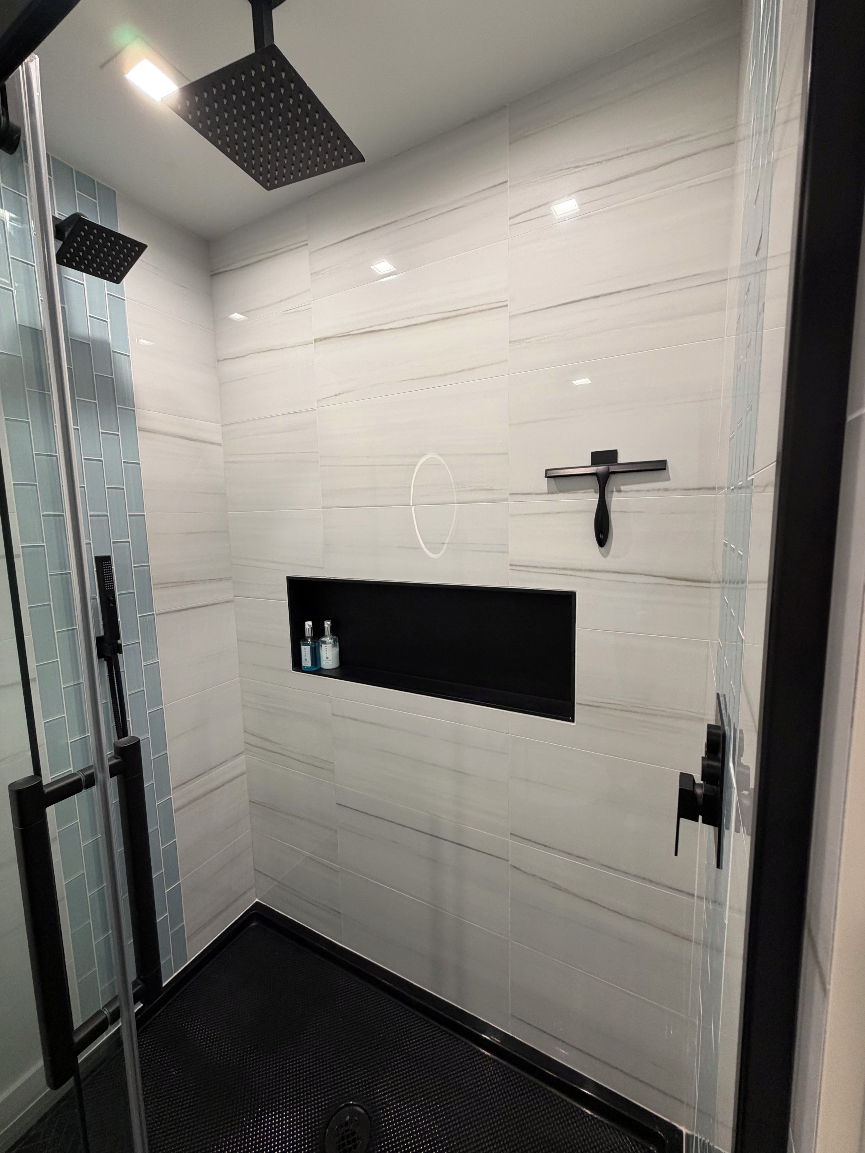 Un baño moderno con cabina de ducha de vidrio, un estante negro con artículos de aseo y un diseño elegante.