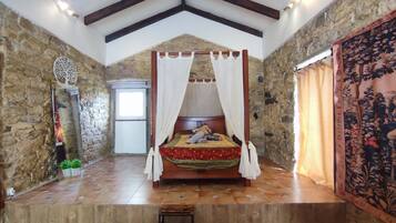 Une chambre avec un mur en pierre, un lit à baldaquin, une petite table et une fenêtre.