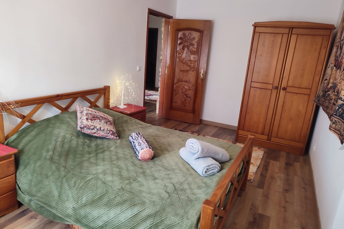 Un dormitorio con una cama de madera, una mesita de noche con lámpara, un armario y una puerta con panel decorativo.