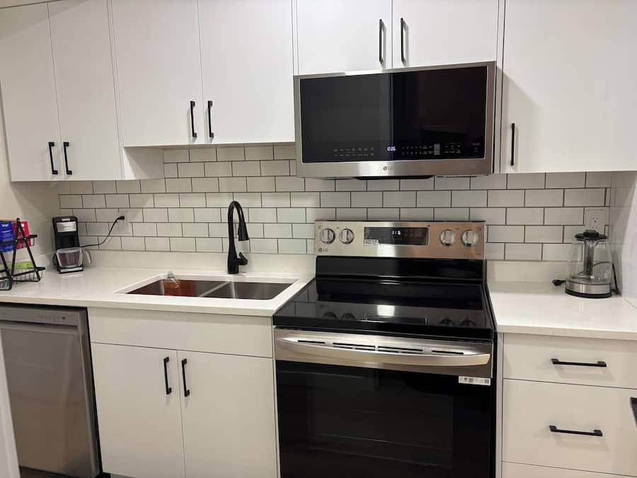 A kitchen with white cabinets, a black microwave, a stainless steel stove, and a coffee maker.