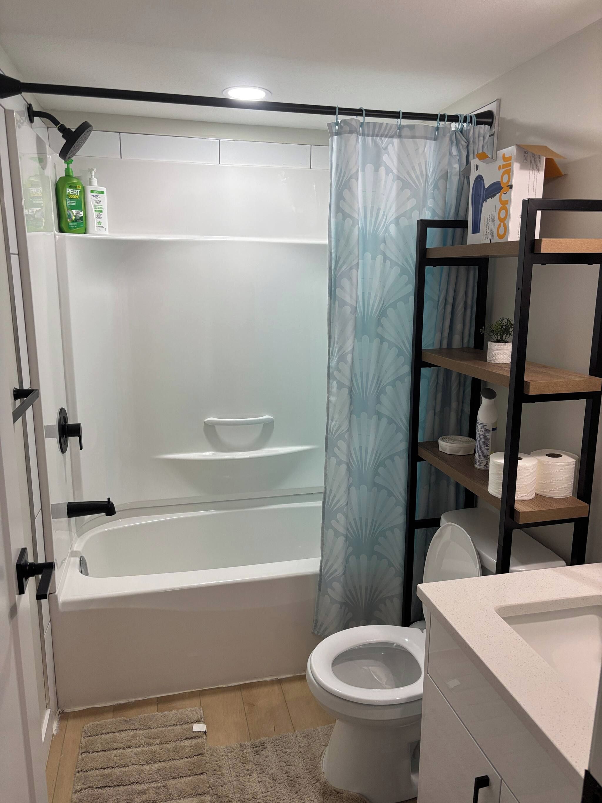 A bathroom with a bathtub, toilet, and shelves with toiletries.