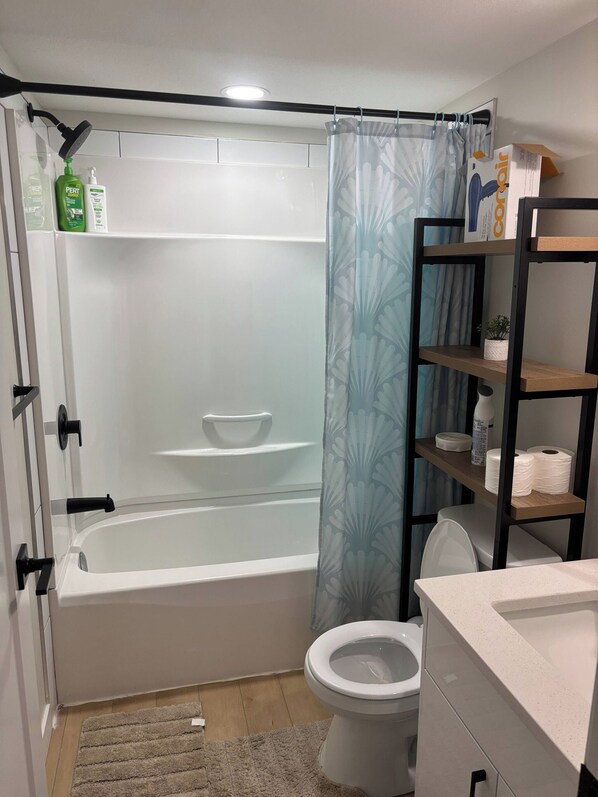 Une salle de bain avec une baignoire, des toilettes et des étagères contenant des articles de toilette.