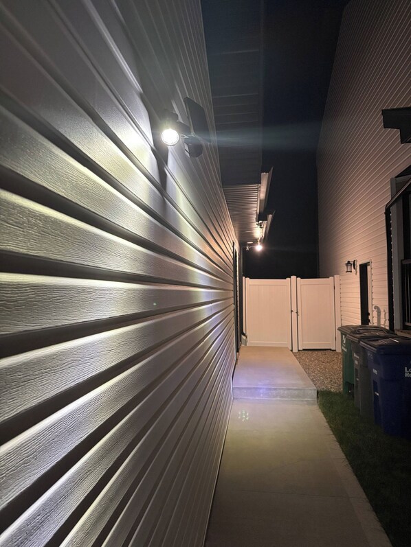 Un pasillo con pared de metal y un camino de hormigón que conduce a una zona vallada.