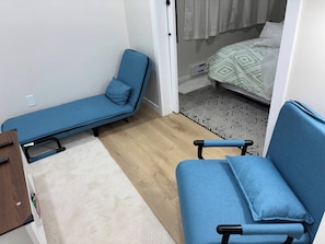 A compact room with a single blue sofa, a small bedside table, and a patterned rug. - Cozy Basement Suite - Home Away From Home (Saskatoon)
