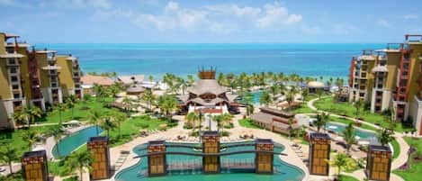 A resort with a central pool, multiple guest buildings, and a view of the ocean.
