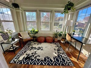 A room with a large window, a black and white patterned rug, a brown leather chair, and a small table with a plant. - Parkside Balcony Condo with Pool Table (Columbus)