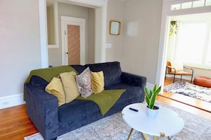 A living room with a dark grey sofa, multiple cushions, a small white table, and a potted plant. - Parkside Balcony Condo with Pool Table (Columbus)