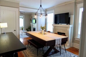 A dining area with a large table, chairs, a chandelier, a fireplace, and a TV mounted above it. - Parkside Balcony Condo with Pool Table (Columbus)