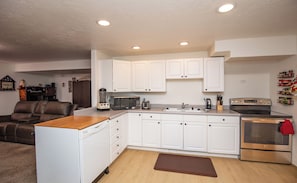 A compact kitchen with white cabinets, a dishwasher, a microwave, a stove, and a coffee maker. - Location, Location, Location (Sandy)