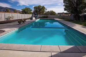 A rectangular swimming pool with clear blue water, surrounded by a wooden fence, concrete deck, and a grassy area. - Location, Location, Location (Sandy)