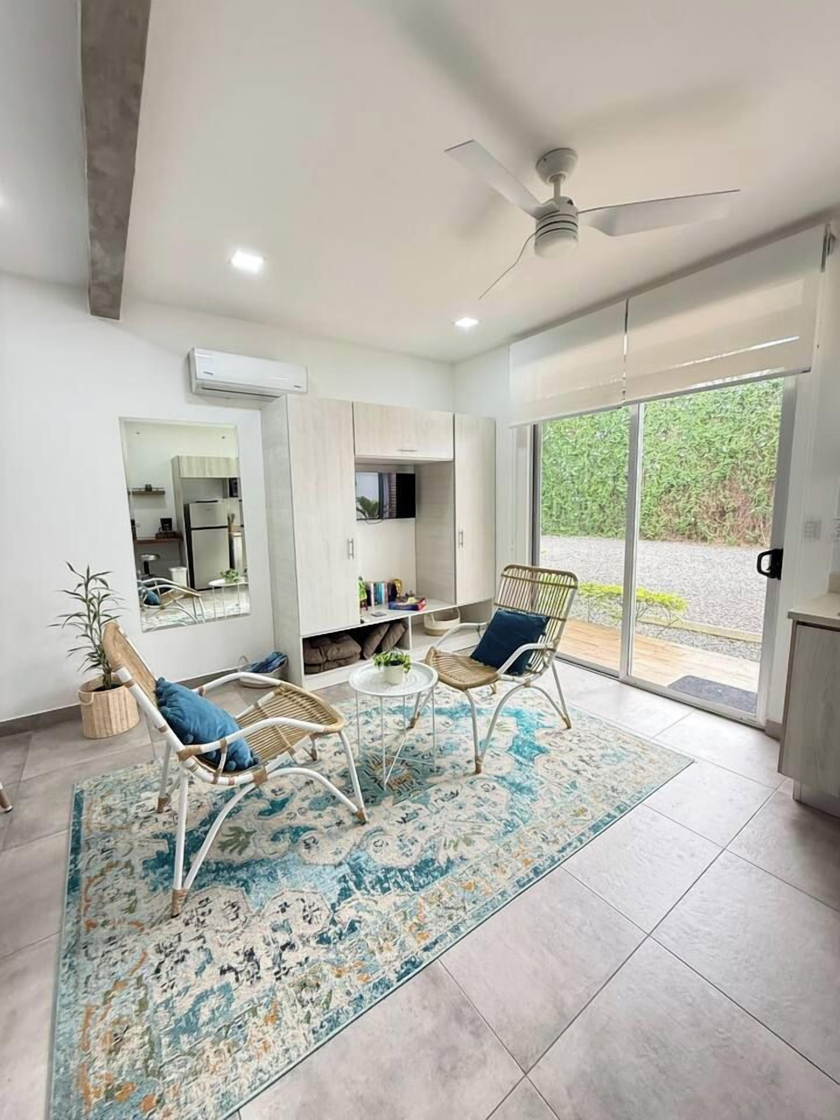 A modern living room with two wicker chairs, a coffee table, and a large window with a view of greenery.
