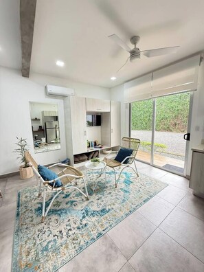 A modern living room with two wicker chairs, a coffee table, and a large window with a view of greenery. - Drift Studio at Costa Lofts - Modern Boho Escape - Apartment (Jaco)