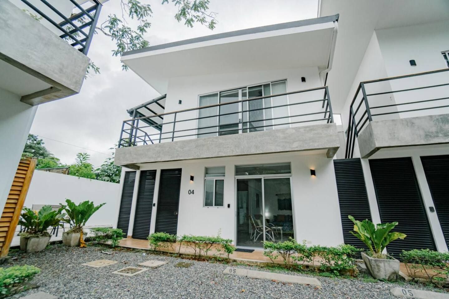 A modern two-story building with a balcony, a covered entrance, and a gravel driveway.