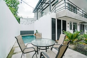 A pool area with a glass table and chairs, surrounded by a white wall and a balcony. - Drift Studio at Costa Lofts - Modern Boho Escape - Apartment (Jaco)