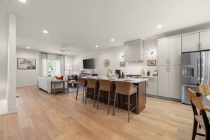A modern kitchen with a central island, bar stools, and a dining area with a sofa and chairs. - 2 Homes Sleeps 18 with 6 Bedrooms, Rooftops + Garage (Nashville)