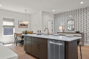 A modern kitchen with a central island, stainless steel appliances, and a patterned wallpaper design. - 2 Homes Sleeps 18 with 6 Bedrooms, Rooftops + Garage (Nashville)