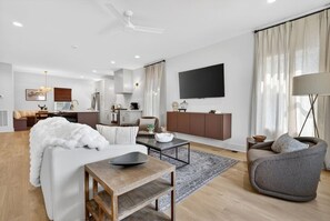 A modern living room with a sofa, armchair, coffee table, and a flat-screen TV mounted on the wall. - 2 Homes, Sleeps 18 - Rooftop, Garage, 3 mi Broadway (Nashville)