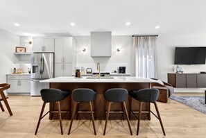 A modern kitchen with a central island, bar stools, a built-in oven, and a flat-screen TV mounted on the wall. - 2 Homes, Sleeps 18 - Rooftop, Garage, 3 mi Broadway (Nashville)