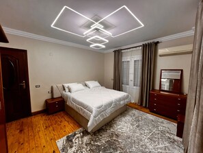 A bedroom with a bed, nightstands, a dresser, a mirror, a window with curtains, and a ceiling light fixture. - 3-bedroom apartment in maadi with air conditioning (Cairo Governorate)