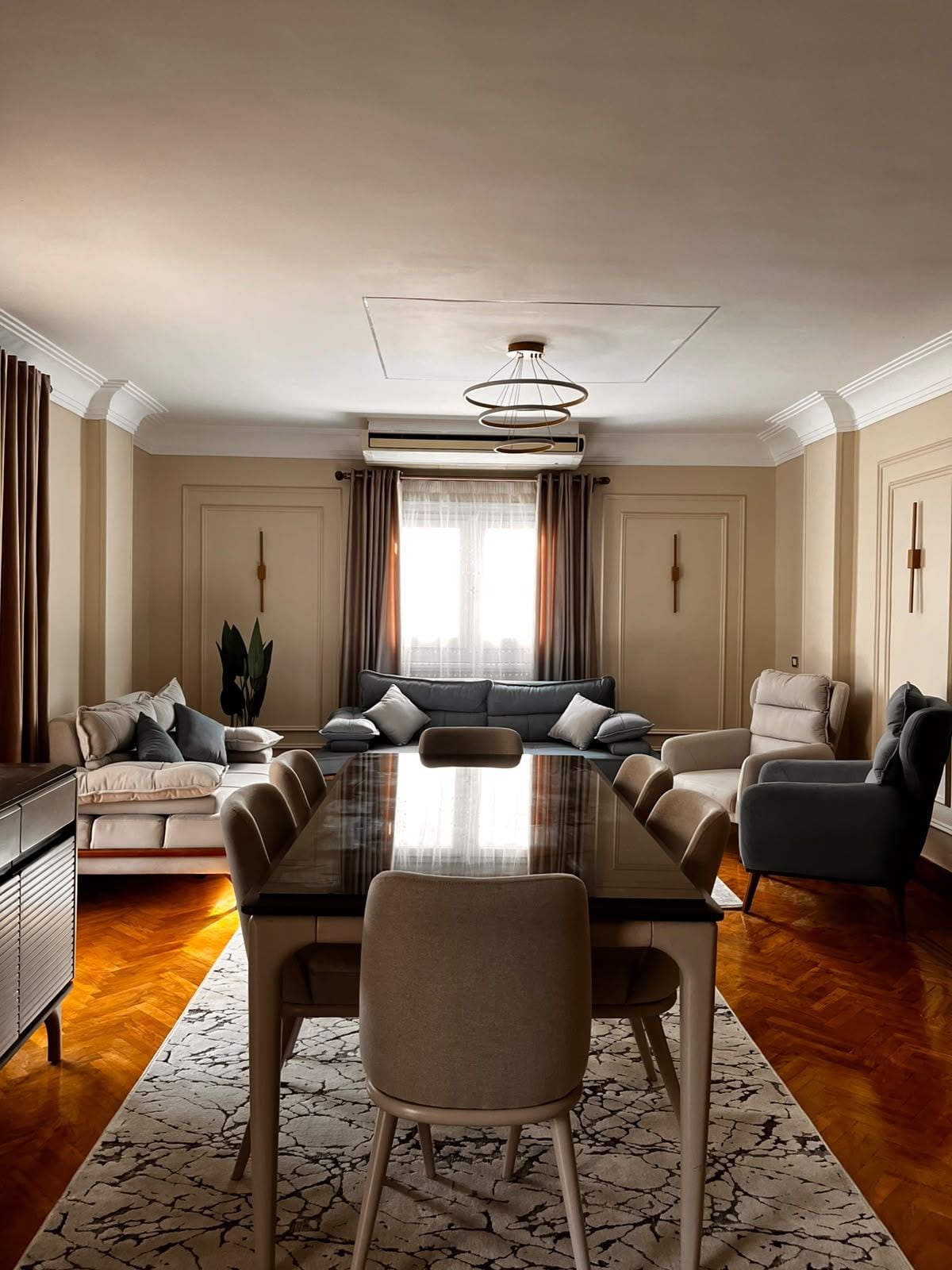 A spacious living room with a large dining table, sofas, and a modern chandelier.