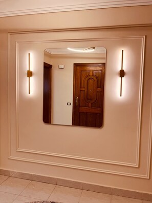 A hallway with a large mirror, two wall-mounted light fixtures, and a wooden door. - 3-bedroom apartment in maadi with air conditioning (Cairo Governorate)