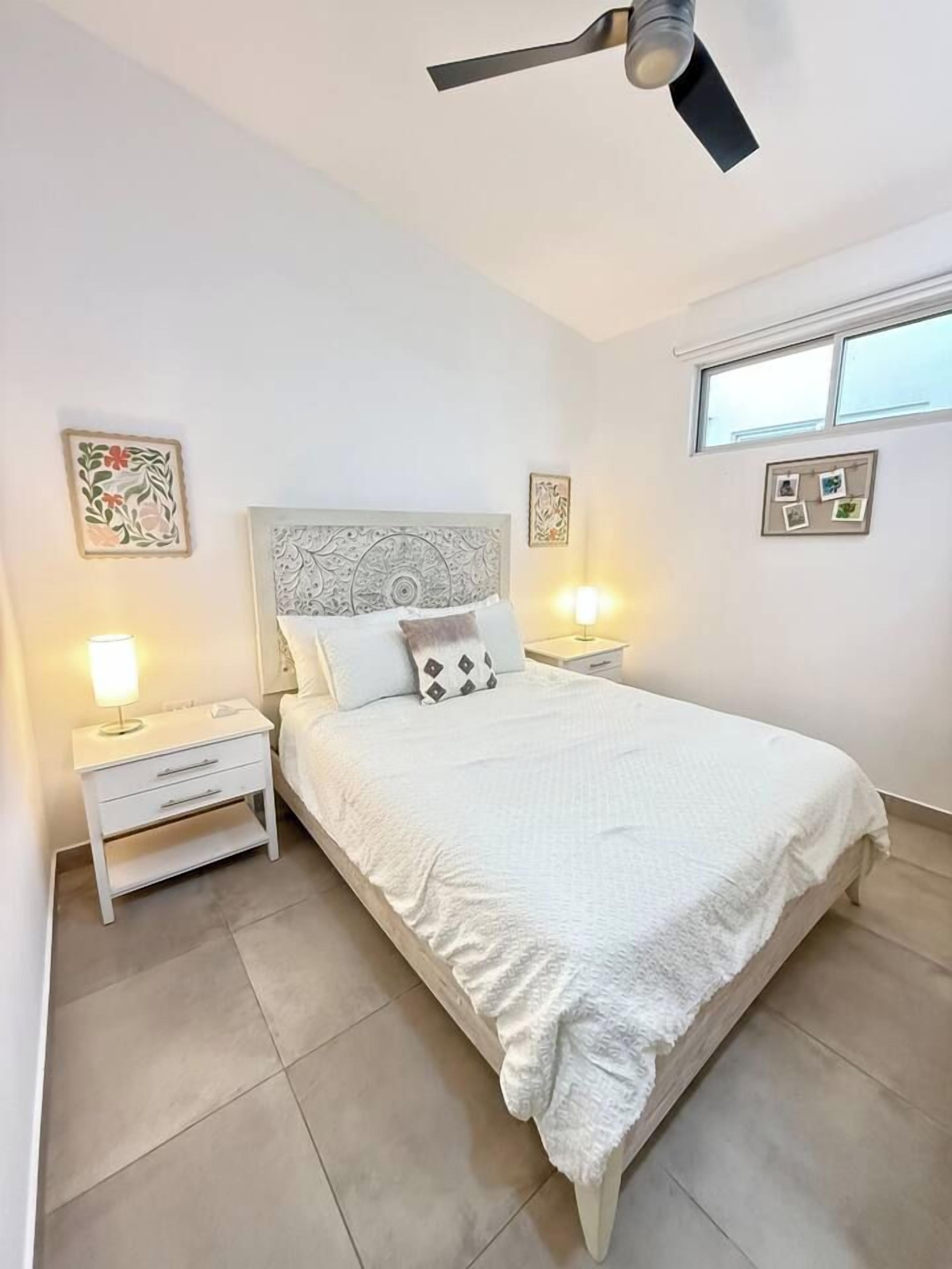 A bedroom with a bed, nightstands, a ceiling fan, and wall art.